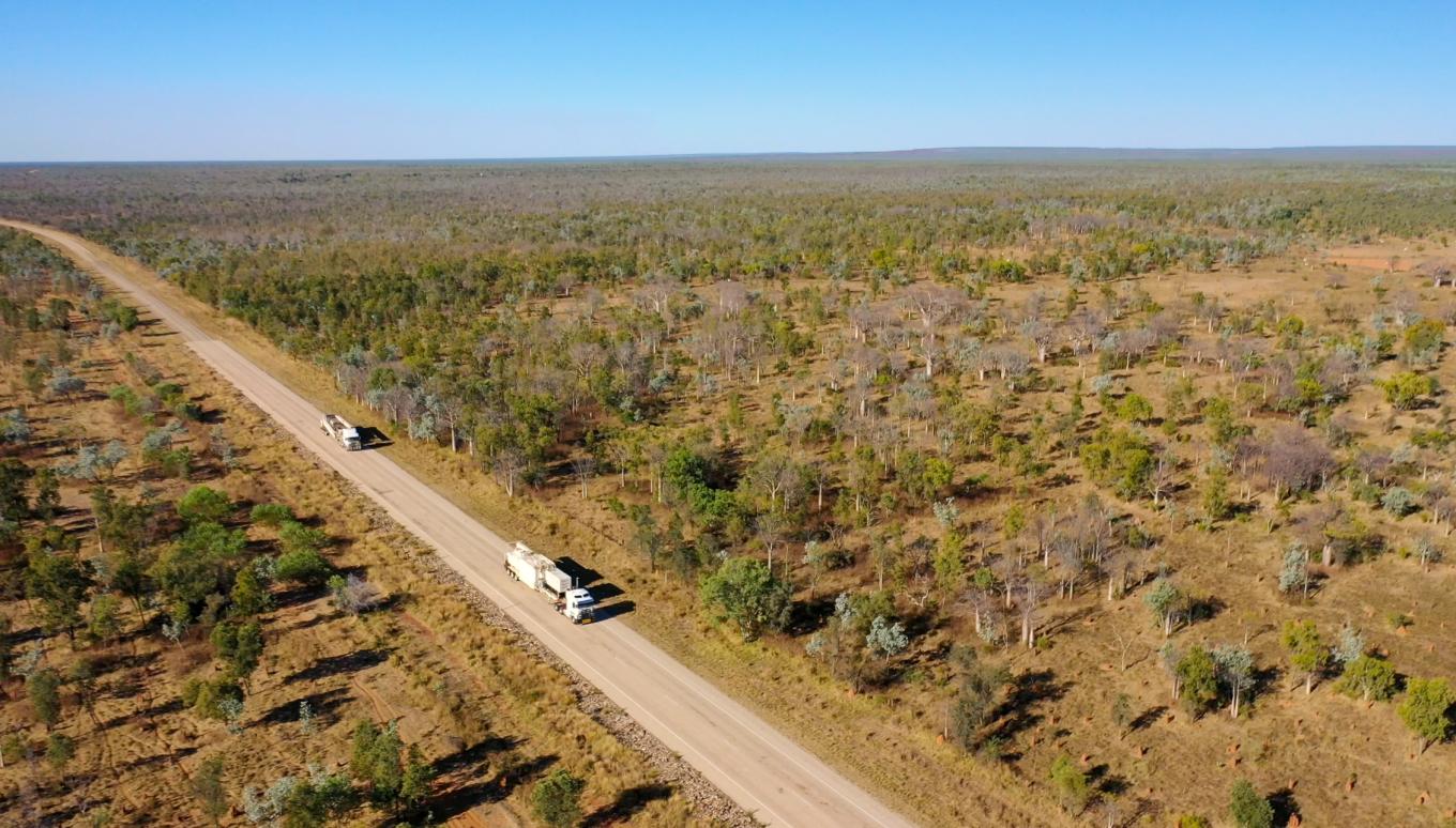 Aerial view of asphalt and equipment transport vehicles travelling along a remote outback road during the Stage 1 Kununurra Airport upgrades, highlighting Colas Australia’s ability to connect regional communities through long-distance project delivery.